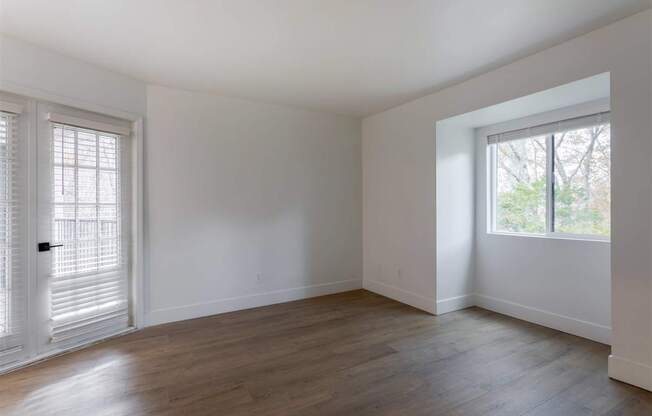 A room with white walls and wooden flooring, with a window on the right side.