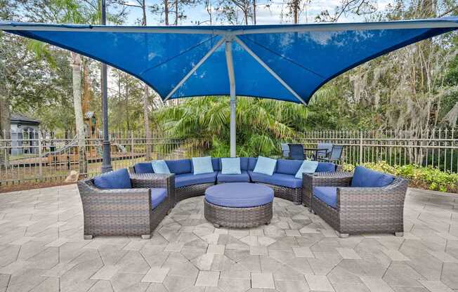 A patio with a blue canopy and grey wicker furniture.