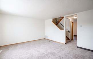 A living room with a carpeted floor and a staircase leading to another room. West Fargo, ND Sheyenne Terrace Townhomes