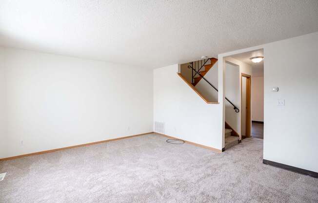 A living room with a carpeted floor and a staircase leading to another room. West Fargo, ND Sheyenne Terrace Townhomes