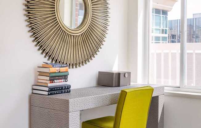 A desk with a yellow chair and a large circular mirror above it.