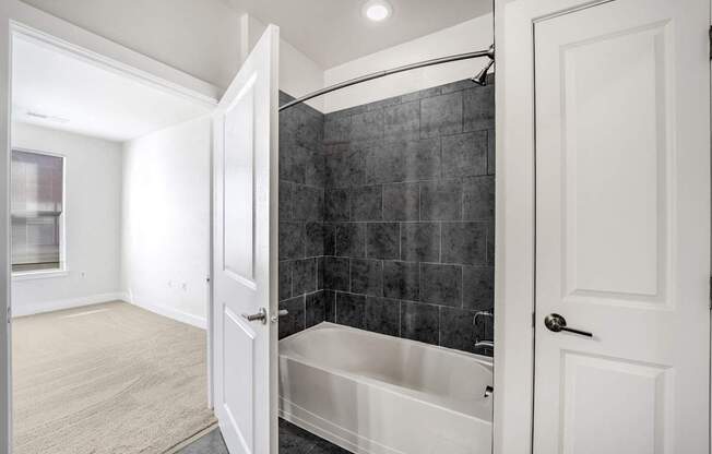 A bathroom with a black tiled shower area and a white bathtub.