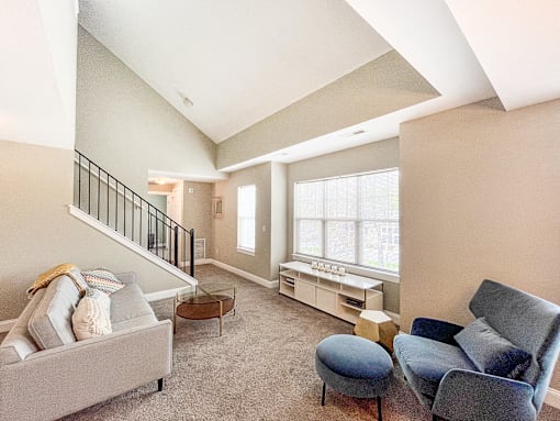 Living area of great room with vaulted ceiling, large, bright windows and stairs to second floor loft