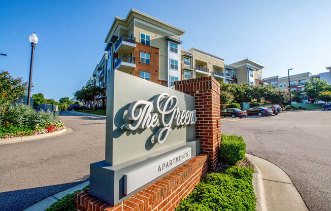 The sign for The Green apartments is in front of a street.