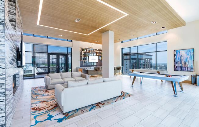 Resident lounge with open seating, a game table, and floor-to-ceiling windows, balancing social energy with room to unwind.