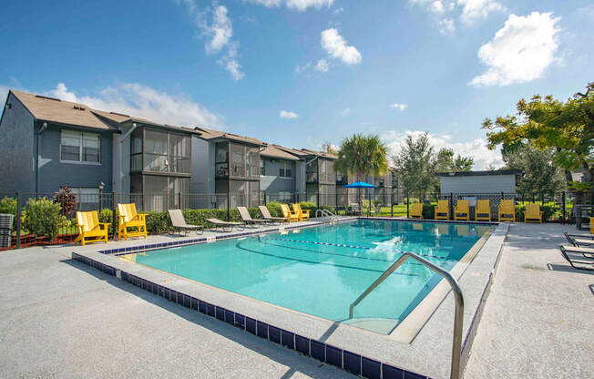A swimming pool surrounded by yellow chairs and apartment buildings.