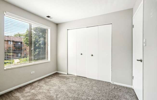 an empty bedroom with a large window and white closets