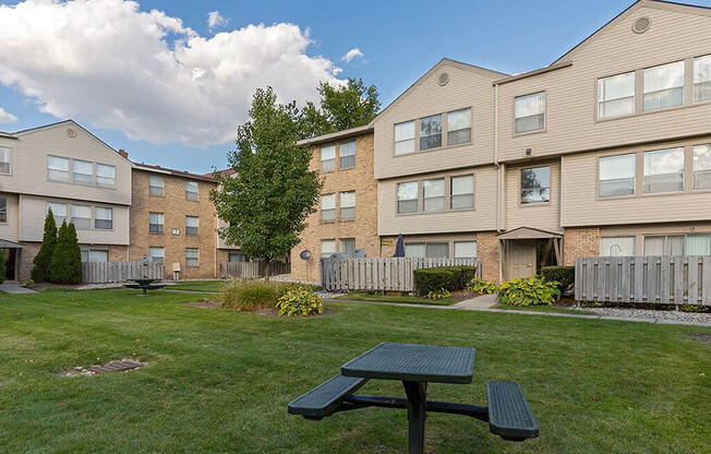 A green picnic table is in the foreground of a grassy area in front of apartment buildings.