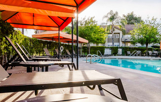 A poolside area with sun loungers and an orange umbrella.