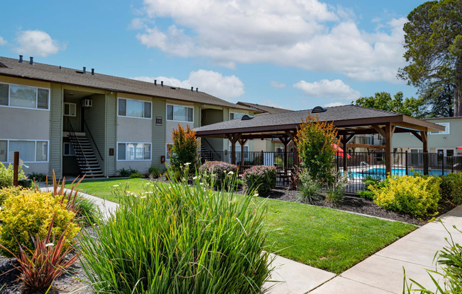 View of exterior building, well landscaped courtyard, gated pool area with covered area with picnic table and seating