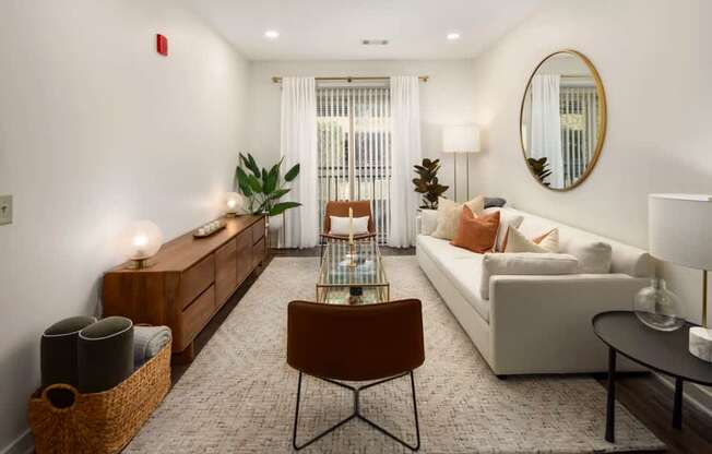 A living room with a brown chair, a white couch, and a round mirror on the wall.