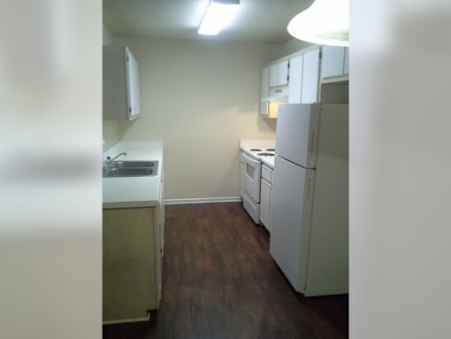 an empty kitchen with white appliances and a refrigerator