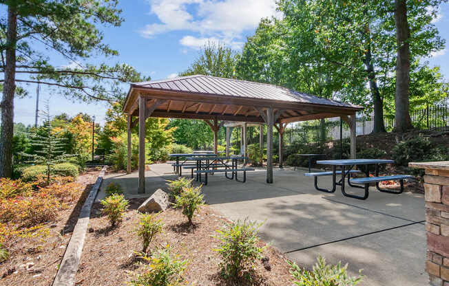 A pavilion with picnic tables is surrounded by trees and shrubs.
