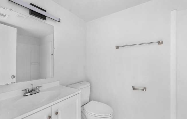 A white bathroom with a toilet, sink, mirror, and towel bar.