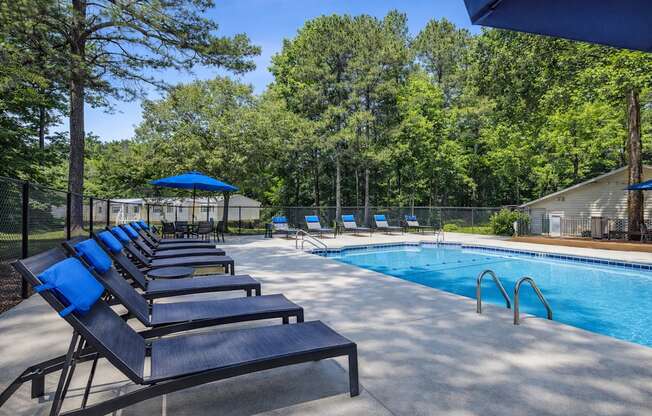 A pool with a blue umbrella and lounge chairs.