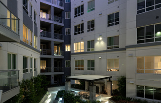 A courtyard surrounded by the interior walls of the apartment complex, with balconies overlooking the landscaping, patio tables and chairs, and dining cabana.