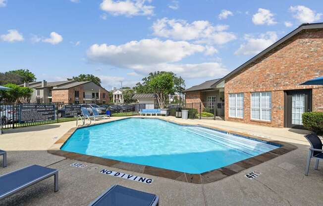 A pool with blue lounge chairs and apartment buildings in the background at The Oaks of Denton Apartments in Denton, TX