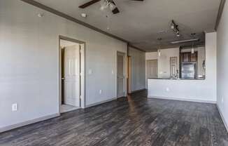 an empty living room with a ceiling fan and a kitchen in the background