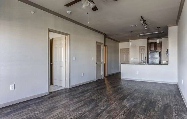 an empty living room with a ceiling fan and a kitchen in the background