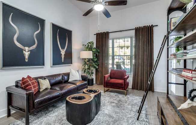 A living room with a black couch, a red chair, and two bull skulls on the wall.
