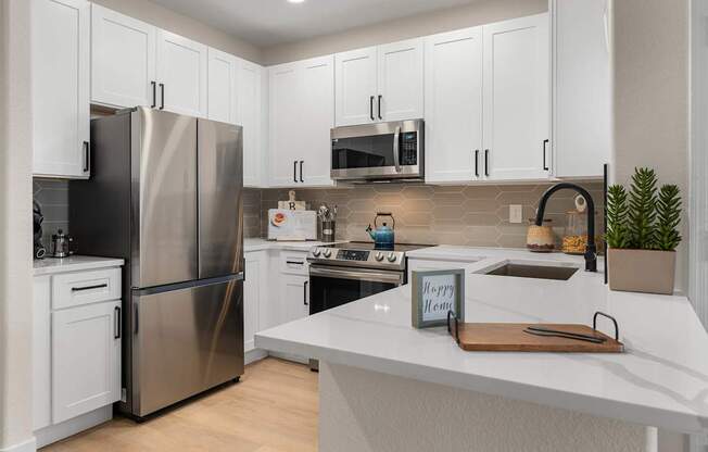 A kitchen with a stainless steel refrigerator, white cabinets, and a white countertop.