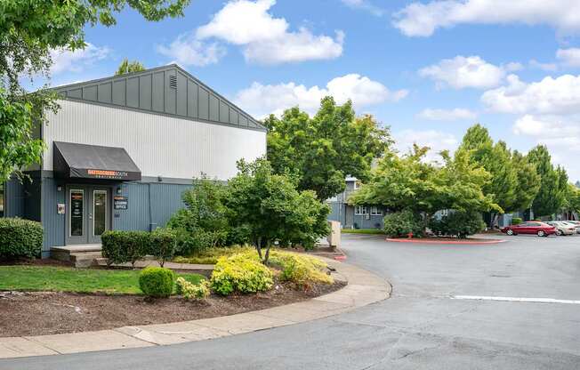 A large grey building with a black awning is surrounded by greenery and a parking lot.