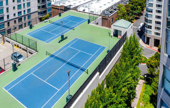 Two tennis courts on a rooftop with trees and buildings around.