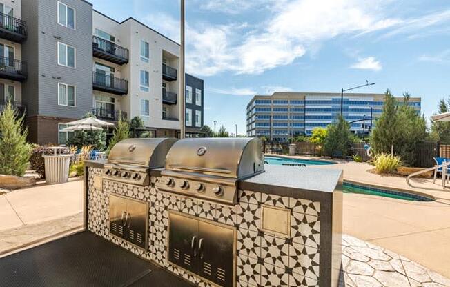 an outdoor grill with a pool and an apartment building in the background