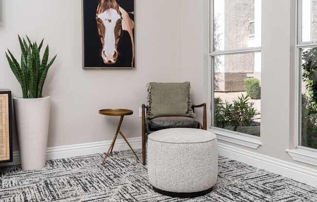 A living room with a chair, ottoman, and a picture of a horse on the wall.