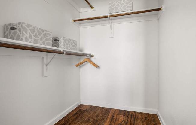A room with a wooden floor and a white wall with a shelf and a hanger.