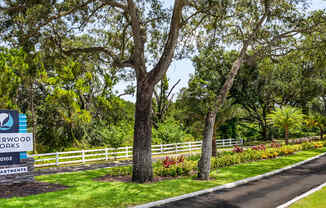 A sign for Sherwood Oaks Apartments stands in front of a tree-lined street.