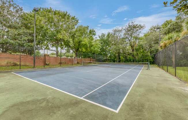 A tennis court surrounded by a fence and trees.