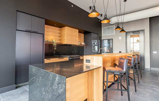 Apartments in Bloomington, MN for Rent - Carbon31 - Kitchen with Contrasting Black and Wooden Tones, Quartz Countertops, a Large Island with Bar Chairs, and Pendant Lights