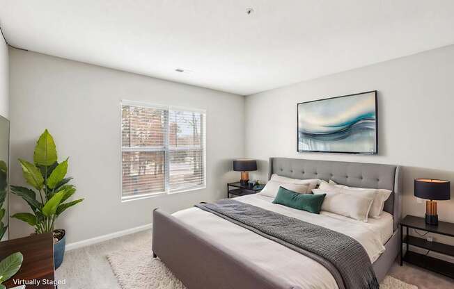 A bedroom with a large bed, a potted plant, and a painting on the wall.