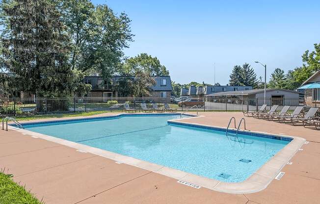 A large outdoor swimming pool surrounded by trees and lounge chairs.