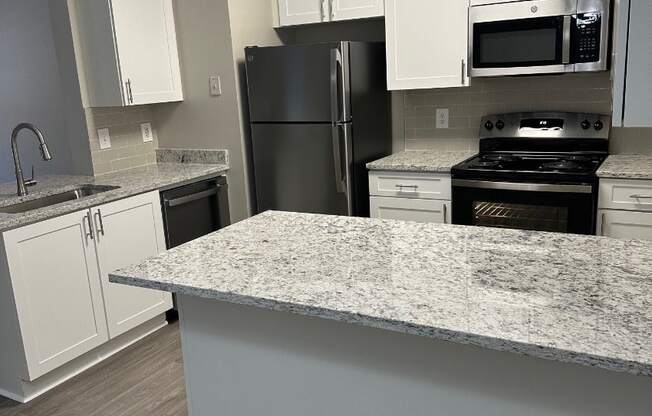 A kitchen with a black refrigerator, white cabinets, and a granite countertop.
