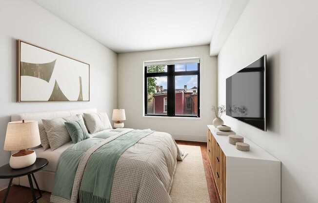 A bedroom with a bed, a television, and a window overlooking a red building.
