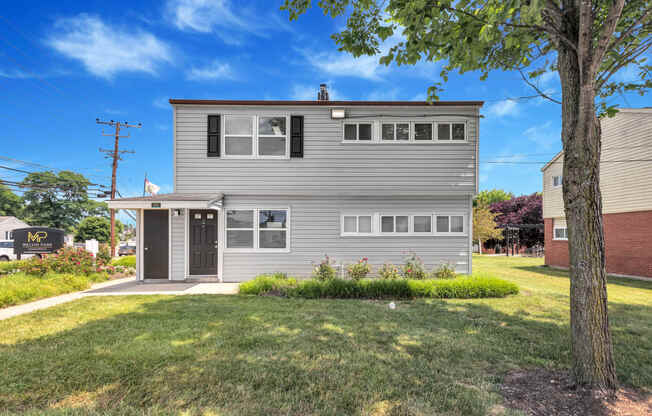 the front of a gray house with a lawn and a tree