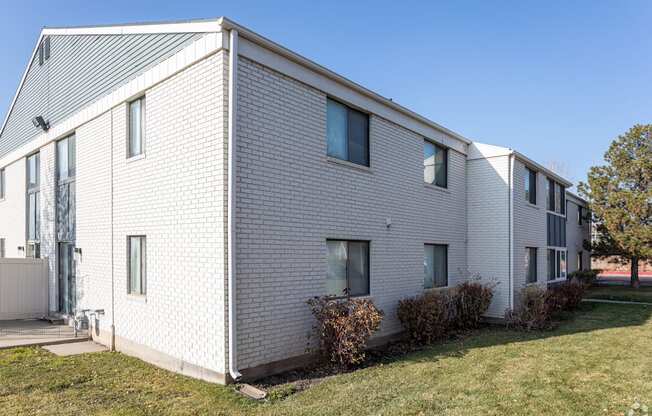 A white brick house with a grey roof and a green lawn in front.