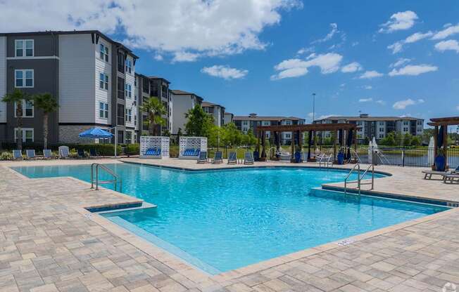 A large swimming pool surrounded by a brick patio and apartment buildings.