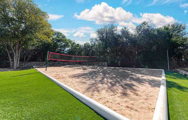 A sand volleyball court with a red net and white boundary lines.