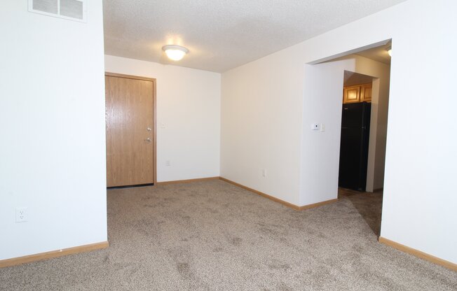 an empty living room with a door to a hallway and a carpeted floor
