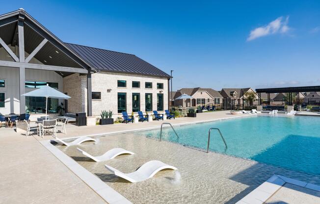 Resort-style pool with shallow lounging, shaded seating, and a modern clubhouse backdrop creates an inviting place to unwind or spend time together.