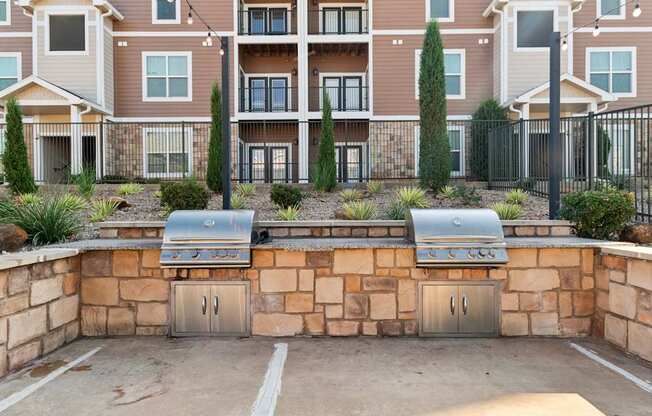 A wall of apartment buildings with a stone wall and grills in front.