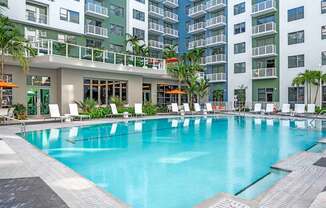 A large swimming pool in front of a building with a balcony.