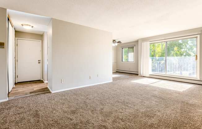 the living room and dining room of an apartment with carpeting and a large window