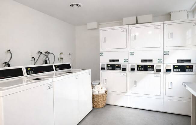 A laundry room with a washer and dryer on the left and a stack of dryers on the right.