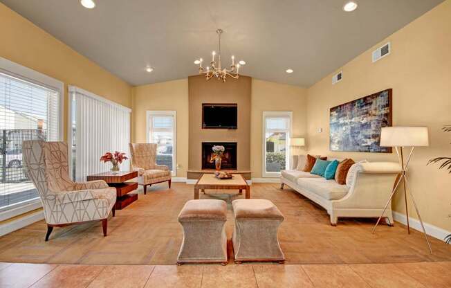 A spacious community lounge here at High Plains with comfortable seating, warm neutral tones, a central fireplace with a mounted TV, and large windows that bring in natural light, creating an inviting space for relaxing or gathering with others.