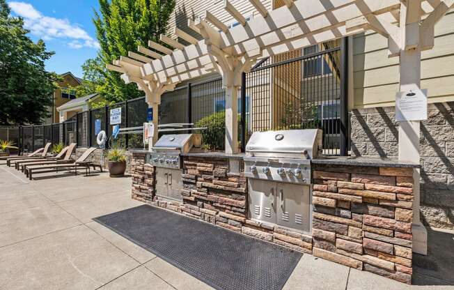 an outdoor barbecue area with two bbq grills and a pergola