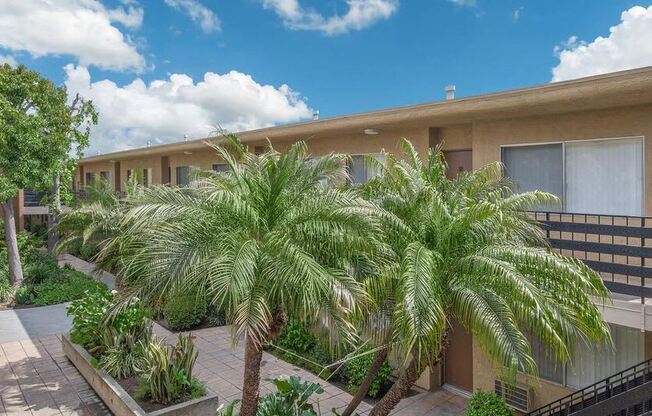 a building with palm trees in front of it at Villa La Paz Apartments, Bellflower, CA